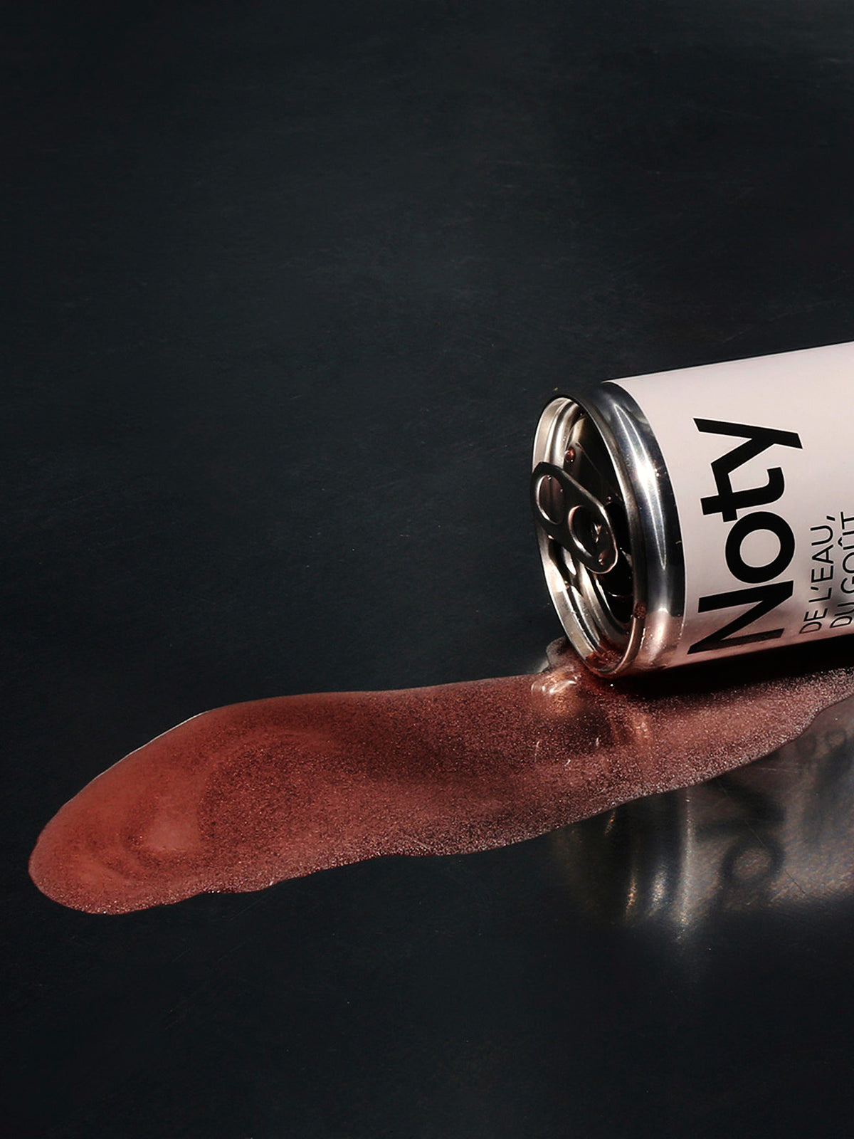 Canette NOTY renversée, soda qui coule sur une surface sombre